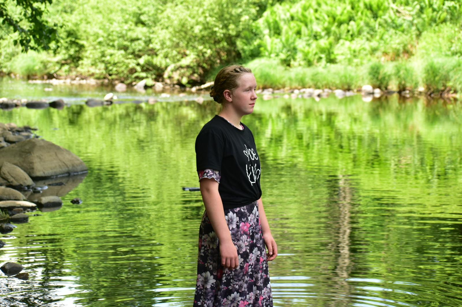 Young woman standing in a calm river, surrounded by lush green forest