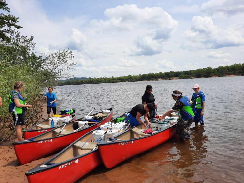 Young women preparing red canoes along the lakeshore