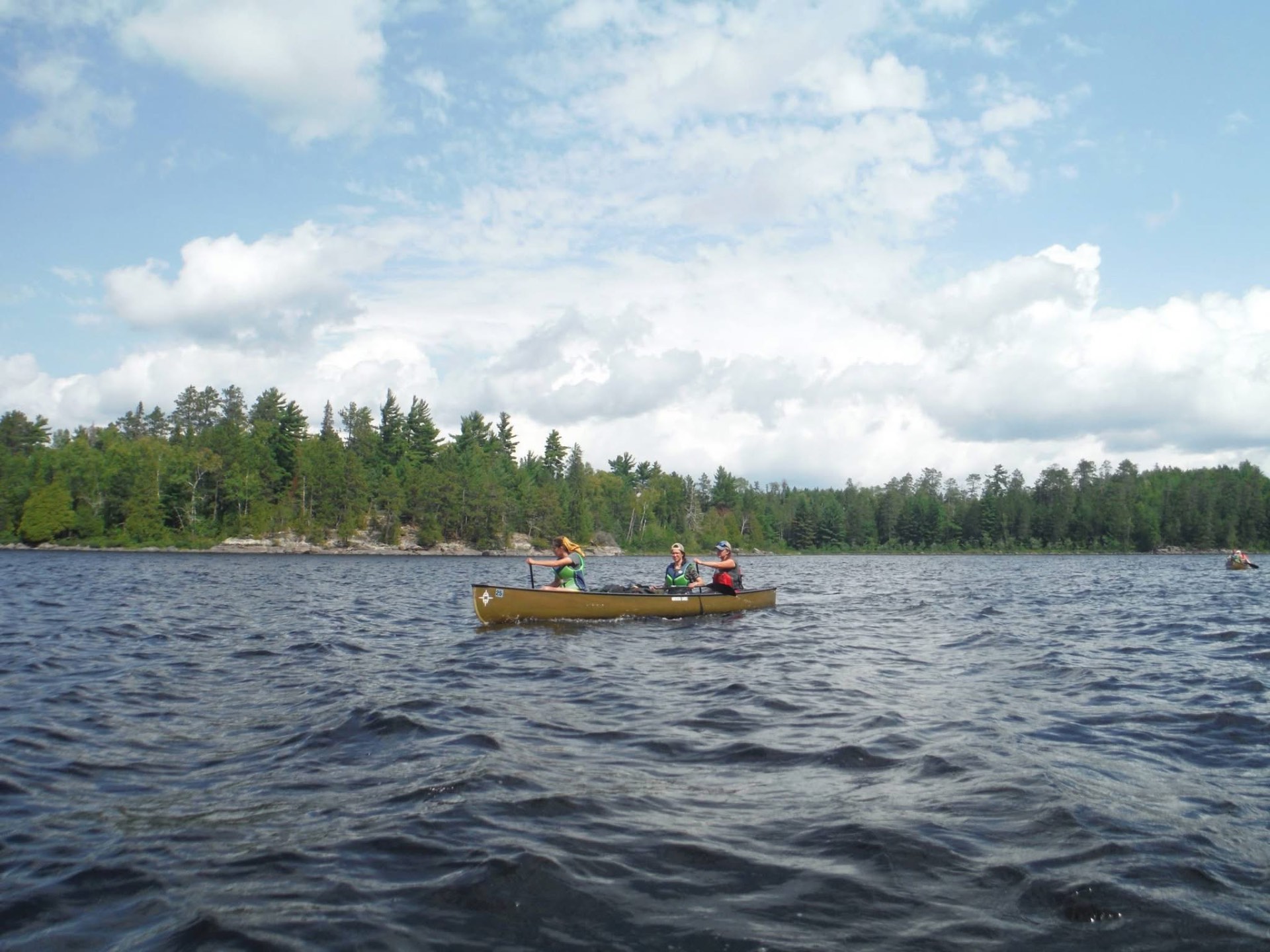 Two young women paddling a canoe across a sunny northern lake
